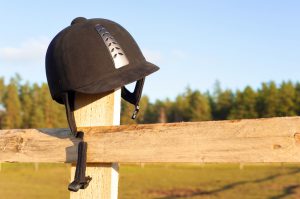 Equestrian equipment - forgotten helmet hanging on the wooden fence with blue sky background. Multicolored summertime outdoors horizontal close-up image.